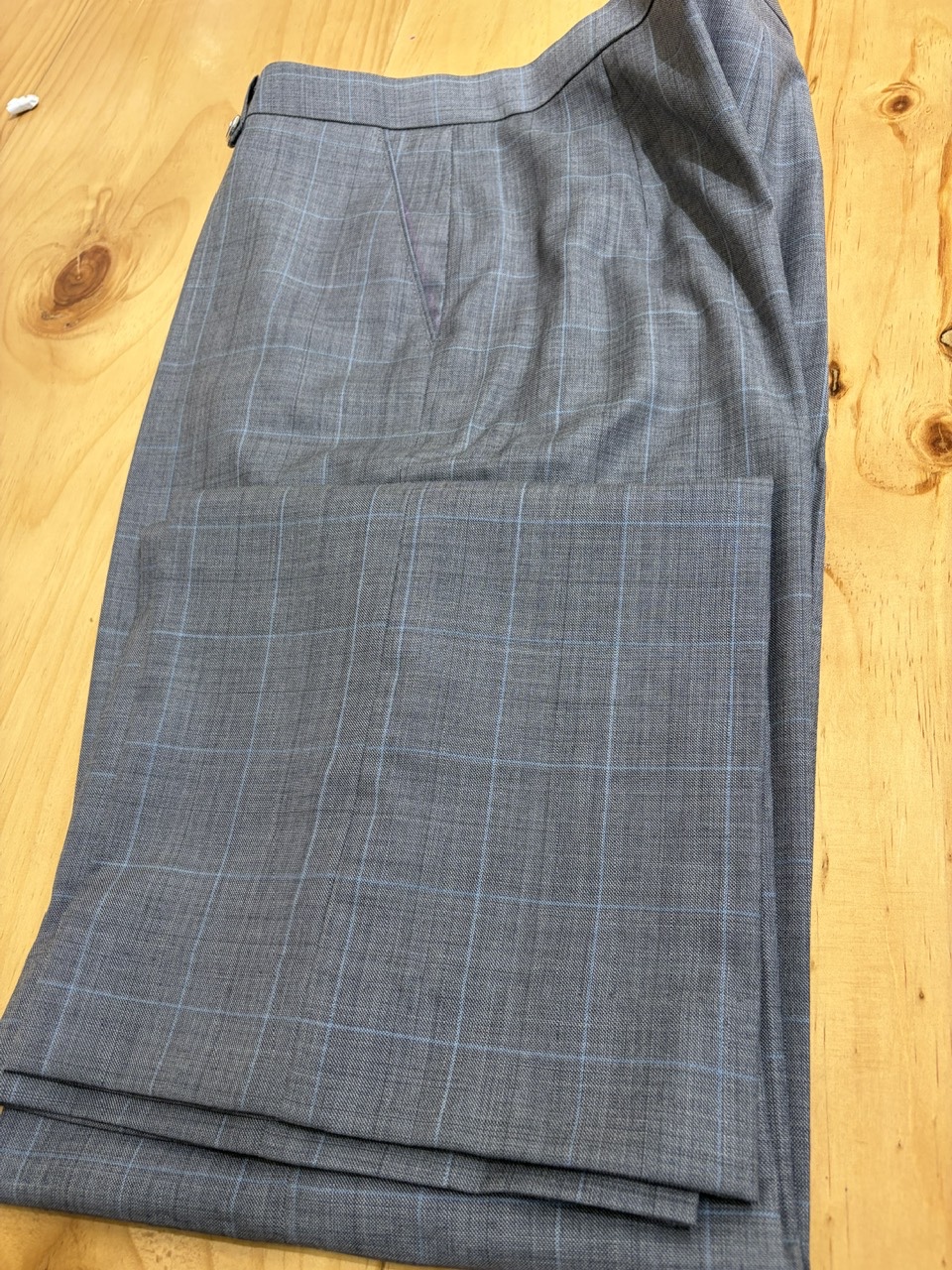 Grey checked tailored trousers folded on wood | Quần may đo caro xám gấp trên nền gỗ